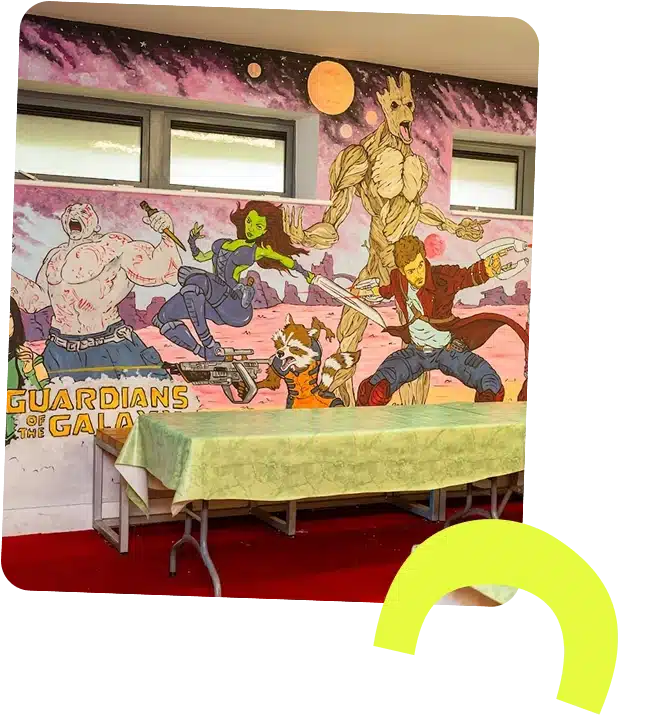 Colourful mural of the Guardians of the Galaxy—Drax, Gamora, Rocket, Groot, and Star-Lord—painted on a wall above folded tables with green tablecloths. About Navan Adventure Centre: a spot where vibrant art meets fun activities.