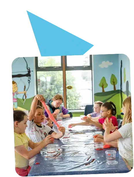Children sit around a table playing with colourful slime in a bright, playful room at Navan Adventure Centre, featuring painted wall murals of trees and a girl with a bow. Sunlight streams through large windows in the background.