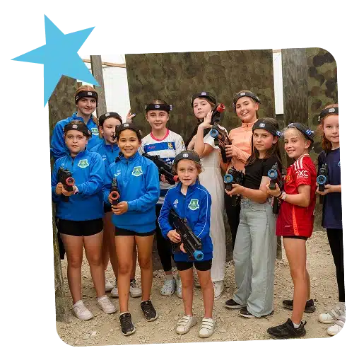 A group of girls and teenagers pose together indoors at Navan Adventure Centre, holding laser tag guns and wearing headbands. They are smiling in their sportswear and casual clothes, with a blue star graphic in the top left corner.