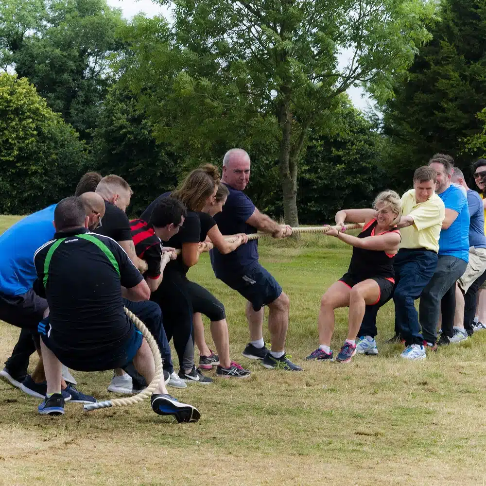A group of people outdoors playing tug of war, each team pulling hard on opposite sides of a rope on a grassy field surrounded by trees—a classic example of Navan team building activities in action.