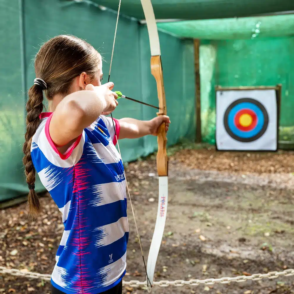 A person with a braided ponytail aims a bow and arrow at a colourful target, wearing a blue and white striped shirt—reminiscent of keen focus seen at Navan indoor archery events.