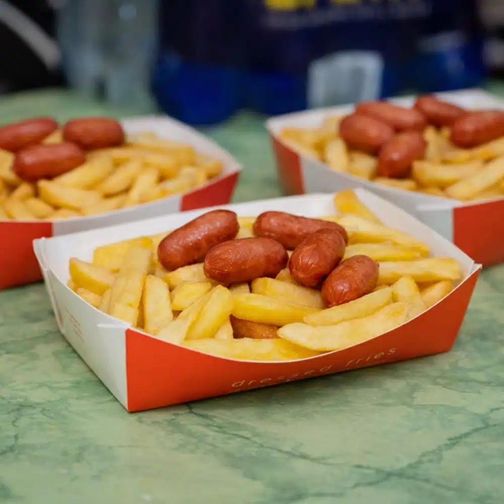 Three trays of chips topped with small sausages sit on a green marble table, ready to fuel the energy of a Navan roller disco party, with the focus on the front tray and two blurred trays in the background.