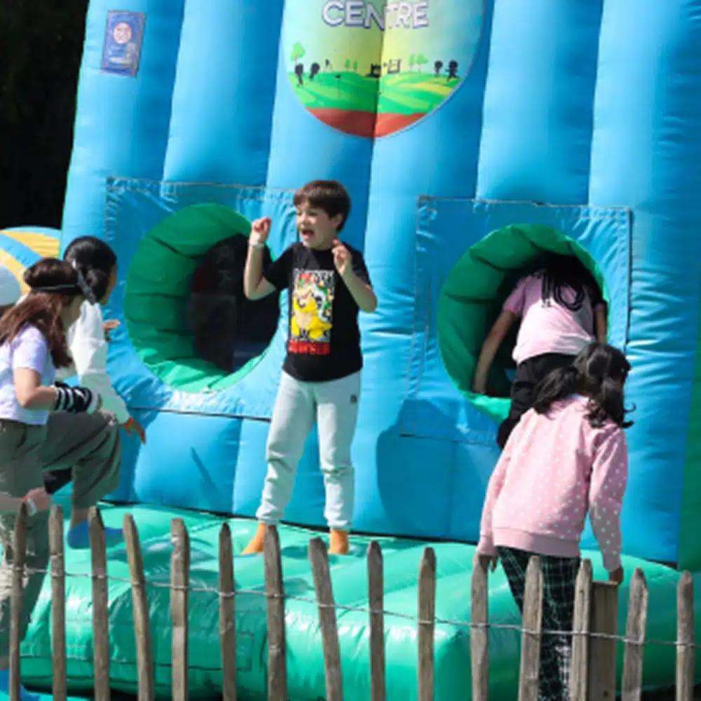 Several children enjoy Navan family activities on a blue inflatable bouncy castle. One boy stands and smiles in front, while others climb or play near circular openings. A wooden fence can be seen in the foreground.